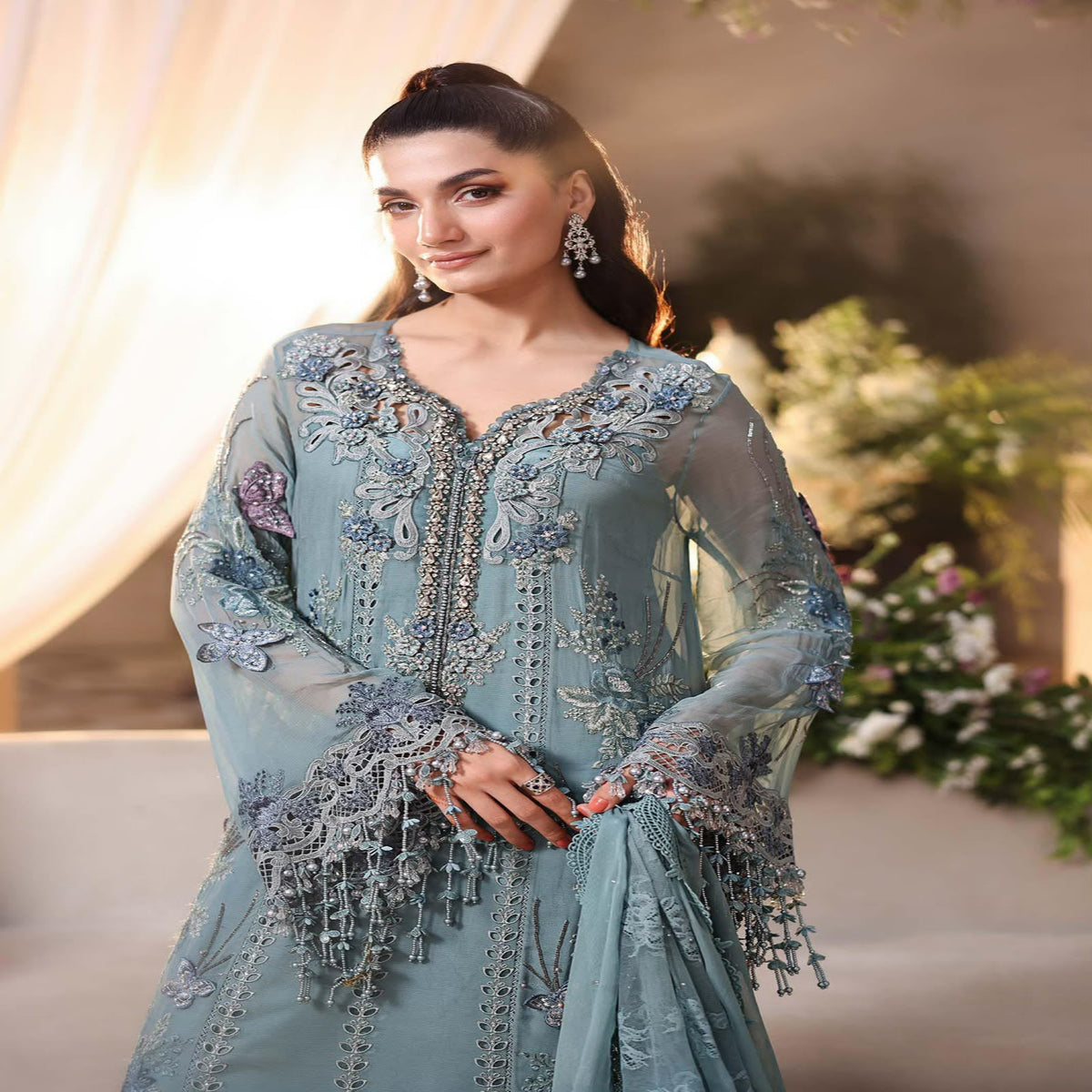 Woman wearing a light blue embroidered dress with floral decorations in an outdoor setting.