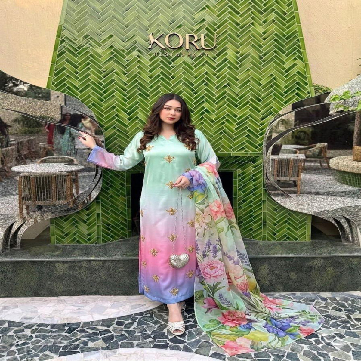 Woman in a colorful dress standing in front of a green 'KORU' sign.