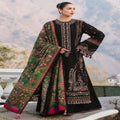 A woman models a traditional black and green embroidered ethnic suit with a matching printed dupatta, set against a blurred outdoor mountain background.