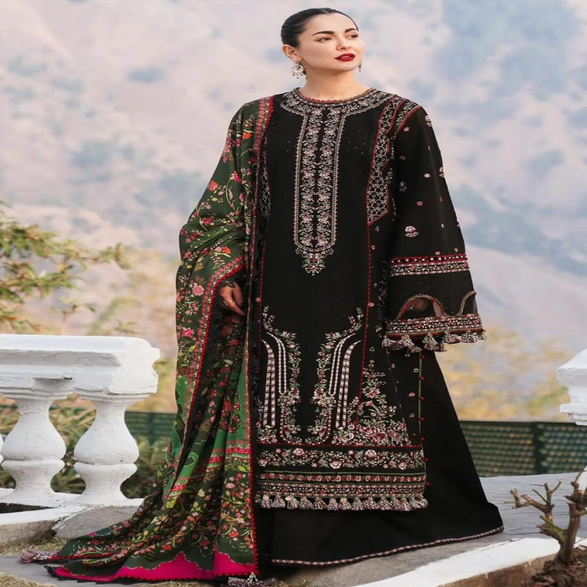Woman wearing a black embroidered outfit with a colorful scarf in an outdoor setting.
