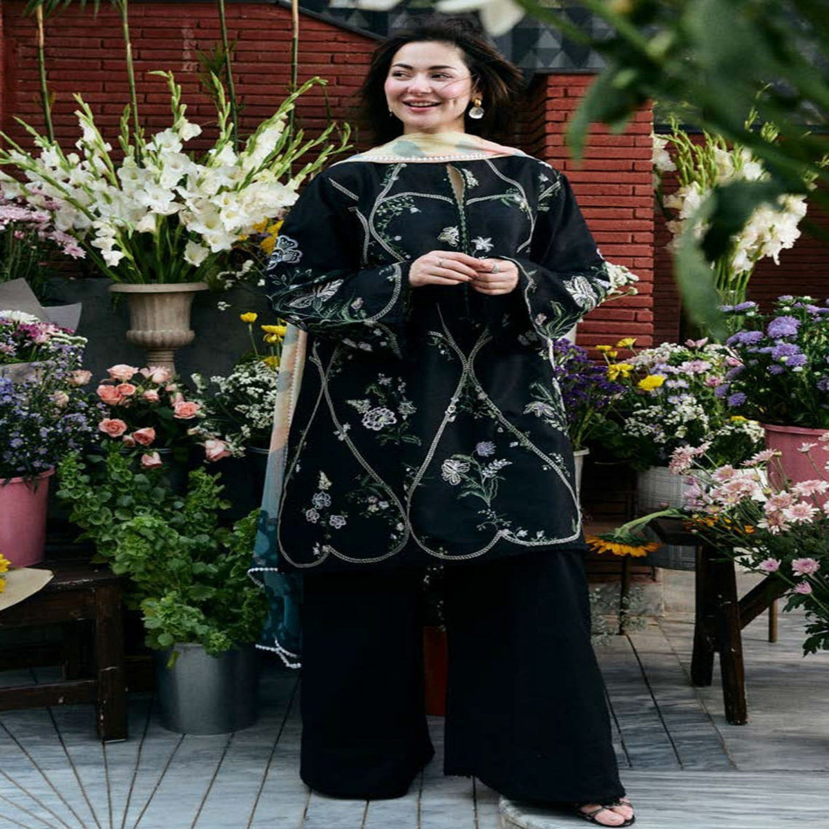 Woman in a black embroidered dress standing among flowers