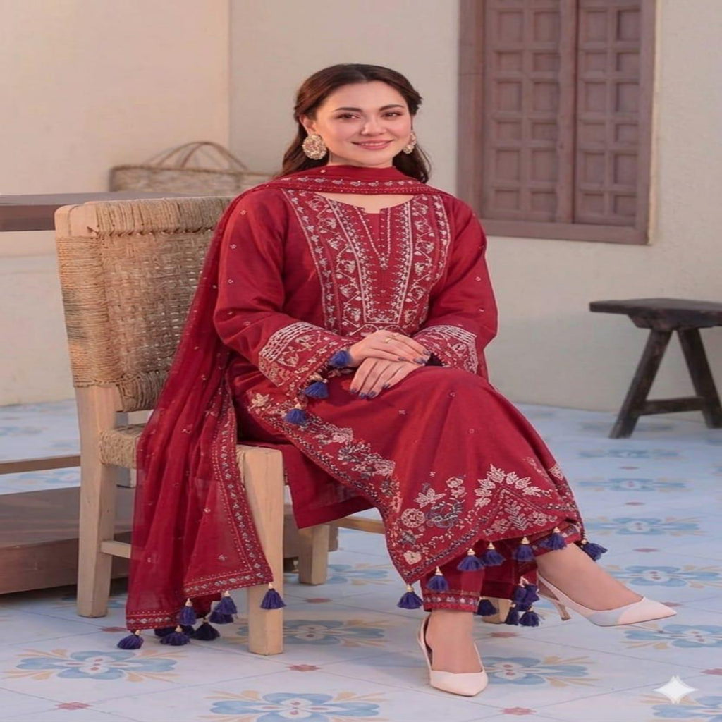 Woman in a red traditional outfit with white patterns and blue tassels sitting on a chair.