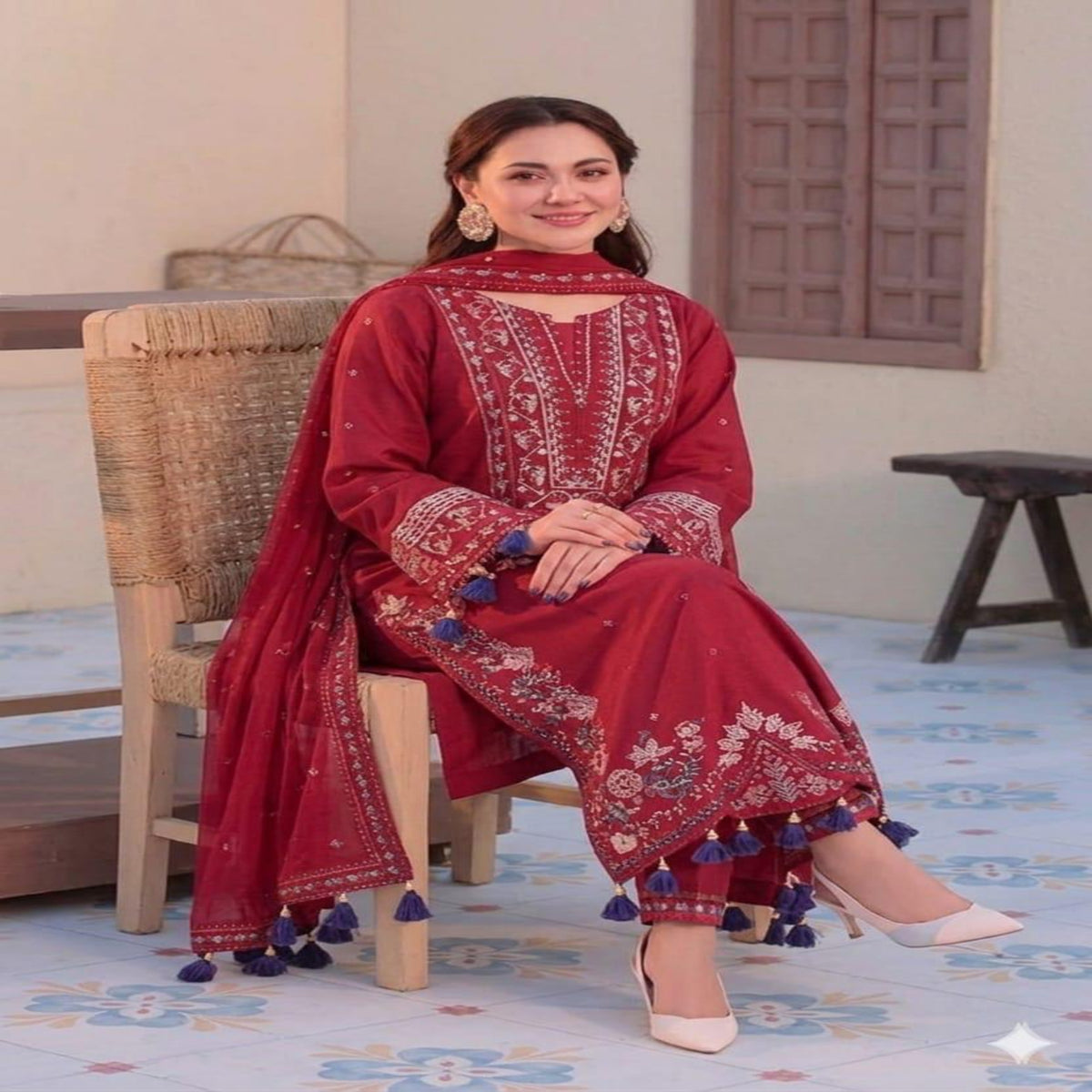Woman in a red traditional outfit with white patterns and blue tassels sitting on a chair.