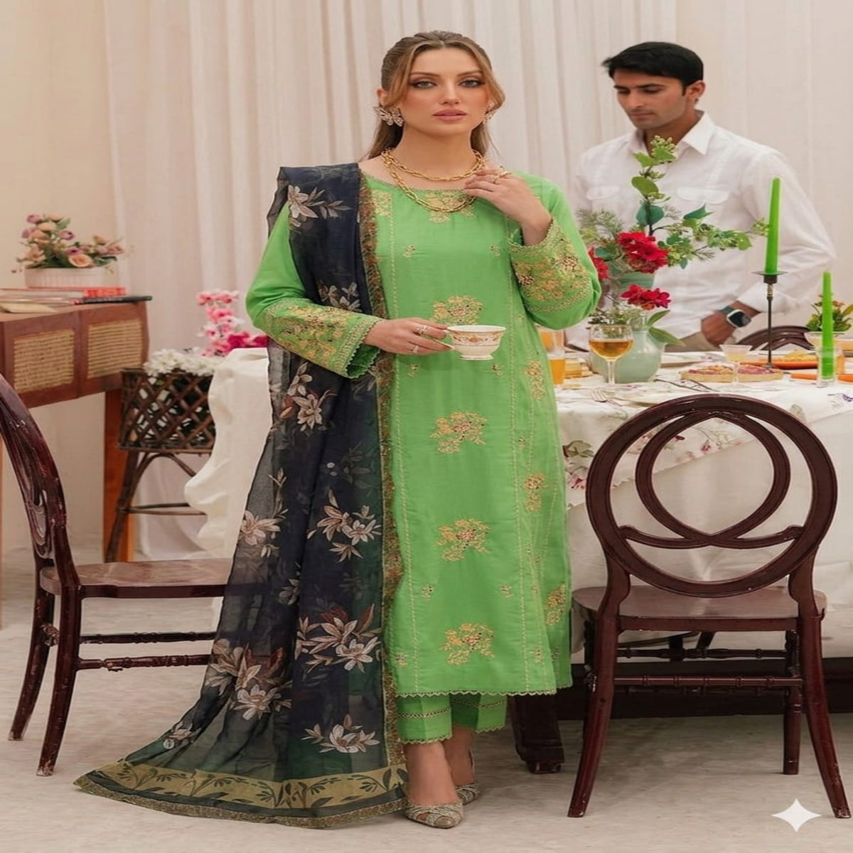 Woman in a green traditional outfit with a man in the background at a decorated table.