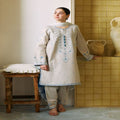 Woman in traditional outfit standing in a room with tiled walls and wooden stool.