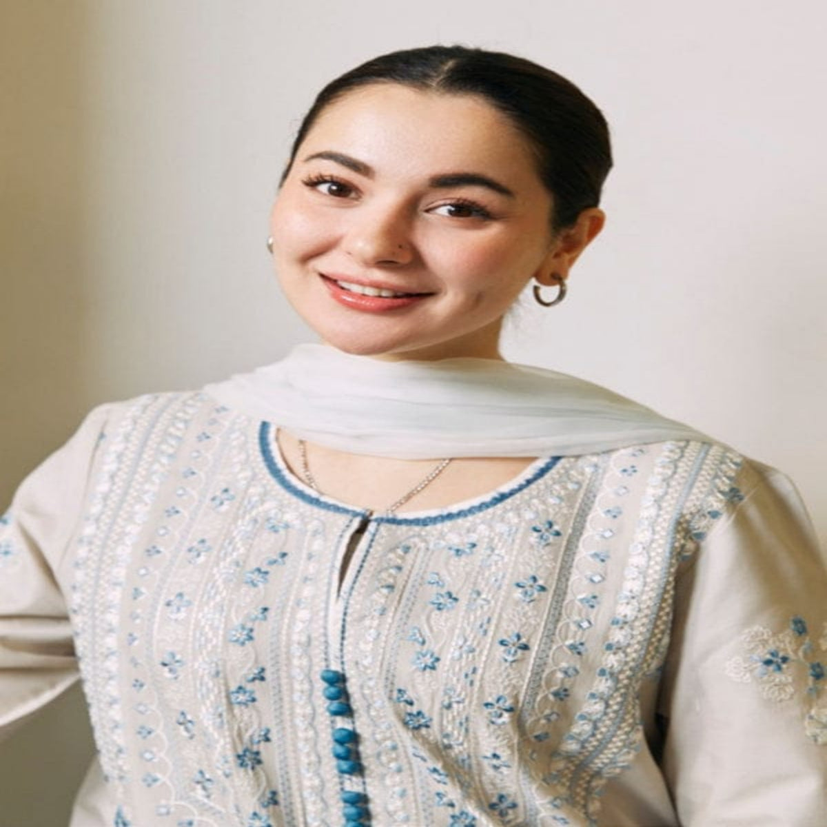Woman wearing a traditional embroidered outfit with a plain background