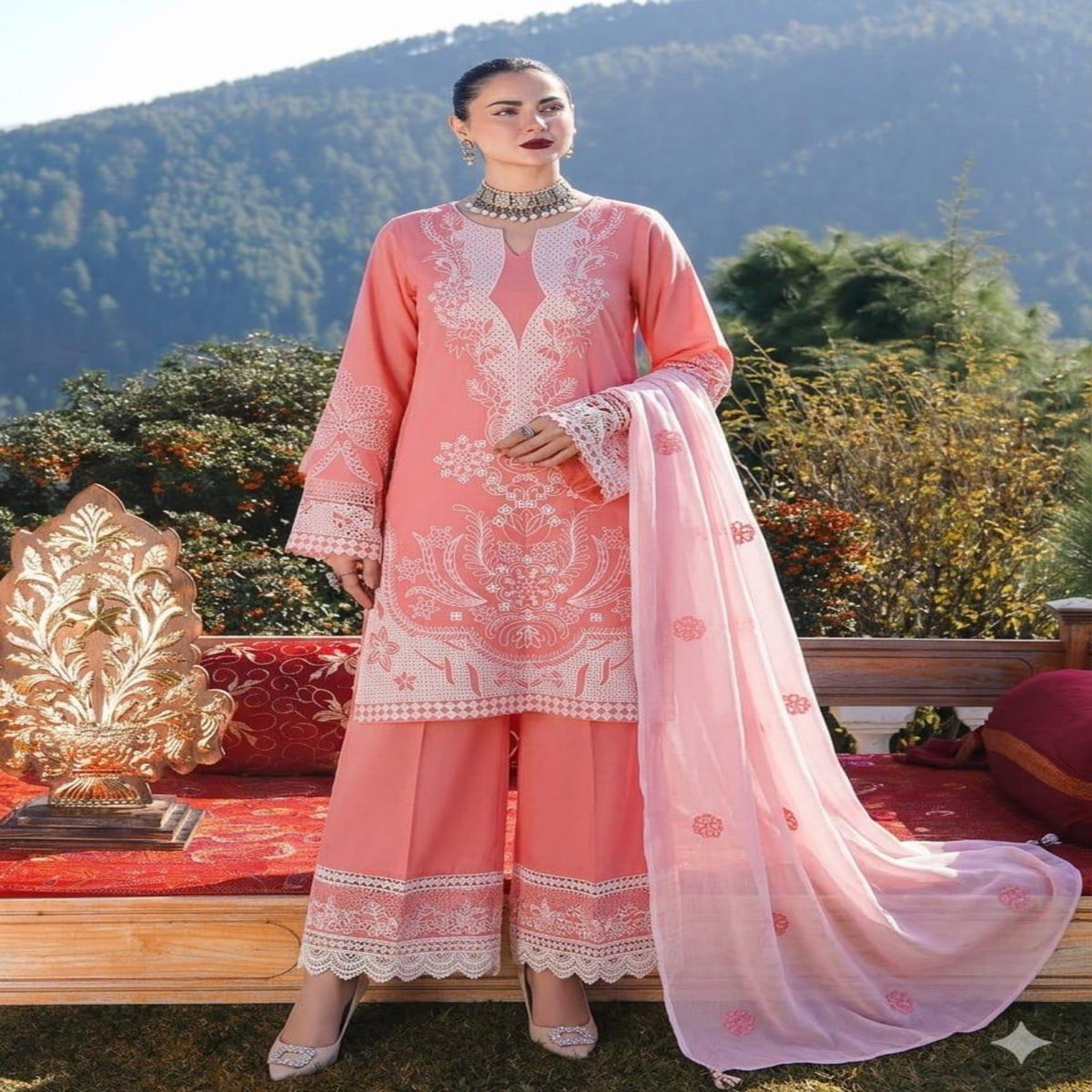 Woman in a pink embroidered outfit standing outdoors with mountains in the background