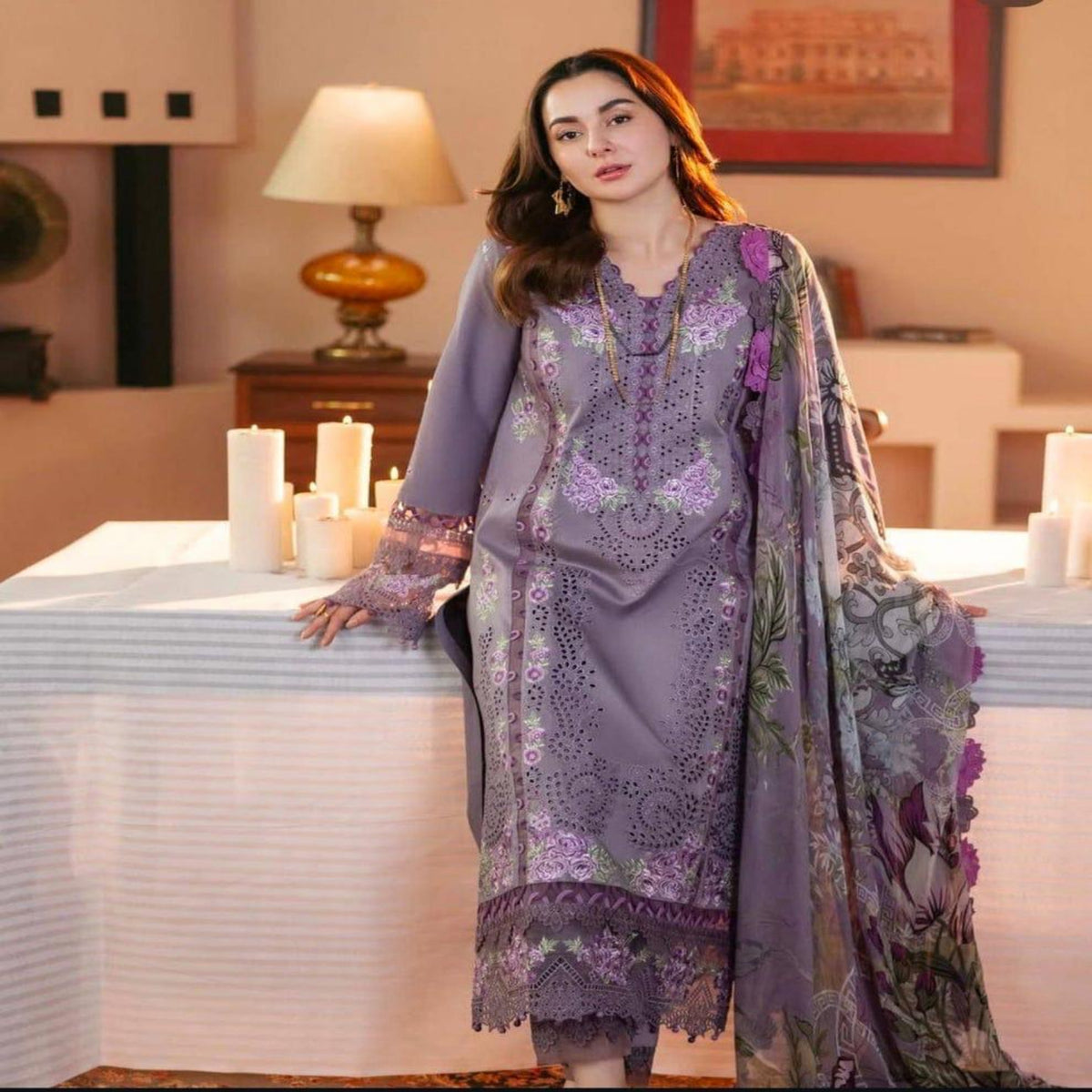 Woman in a purple embroidered outfit standing in a decorated room with candles and a lamp.