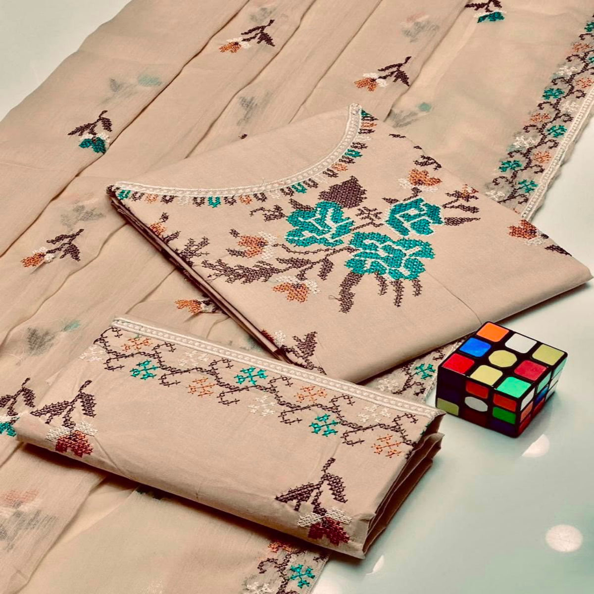 Embroidered fabric with floral patterns on a light surface next to a Rubik's cube.