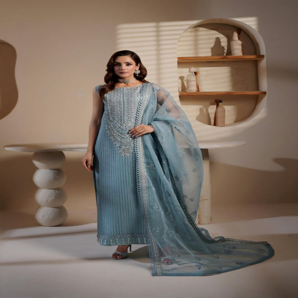 Woman in a light blue traditional outfit standing in a minimalistic room.