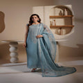 Woman in a light blue traditional outfit standing in a minimalistic room.