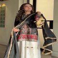 Woman wearing a traditional black and white outfit with intricate designs, standing indoors.