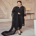 Woman in a black embroidered outfit standing in an elegant interior setting.