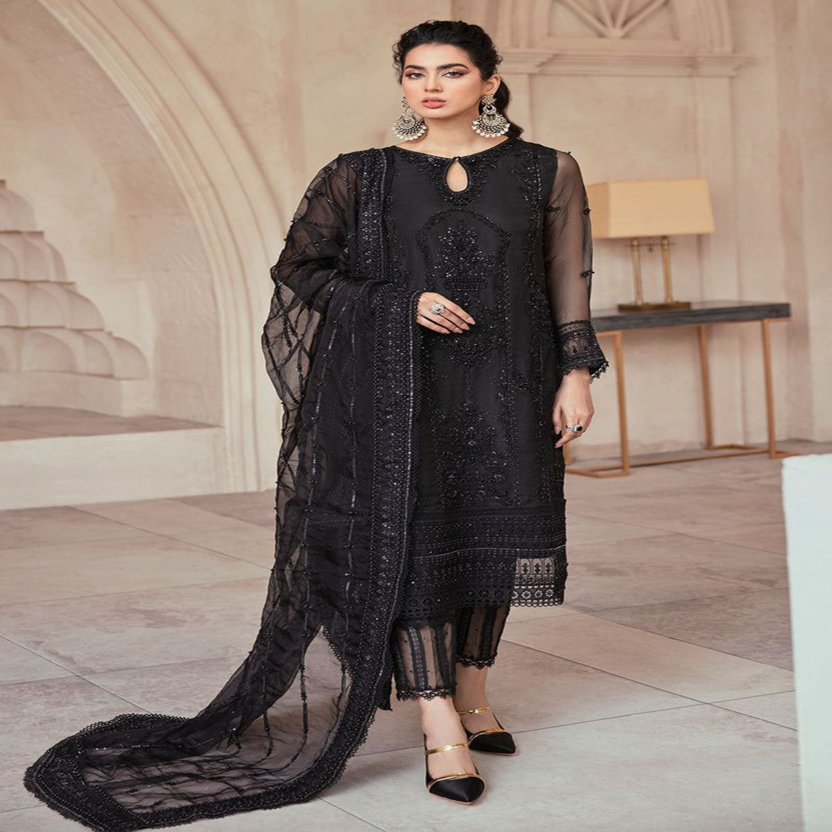Woman in a black embroidered outfit standing in an elegant interior setting.