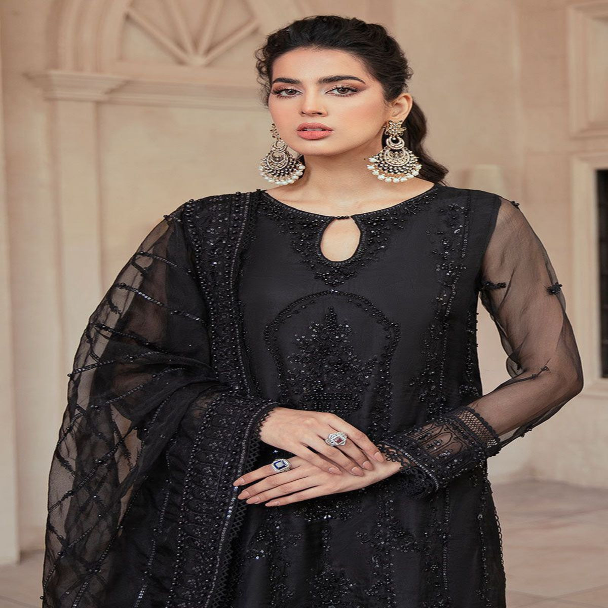 Woman wearing a black embroidered outfit with sheer sleeves in an indoor setting