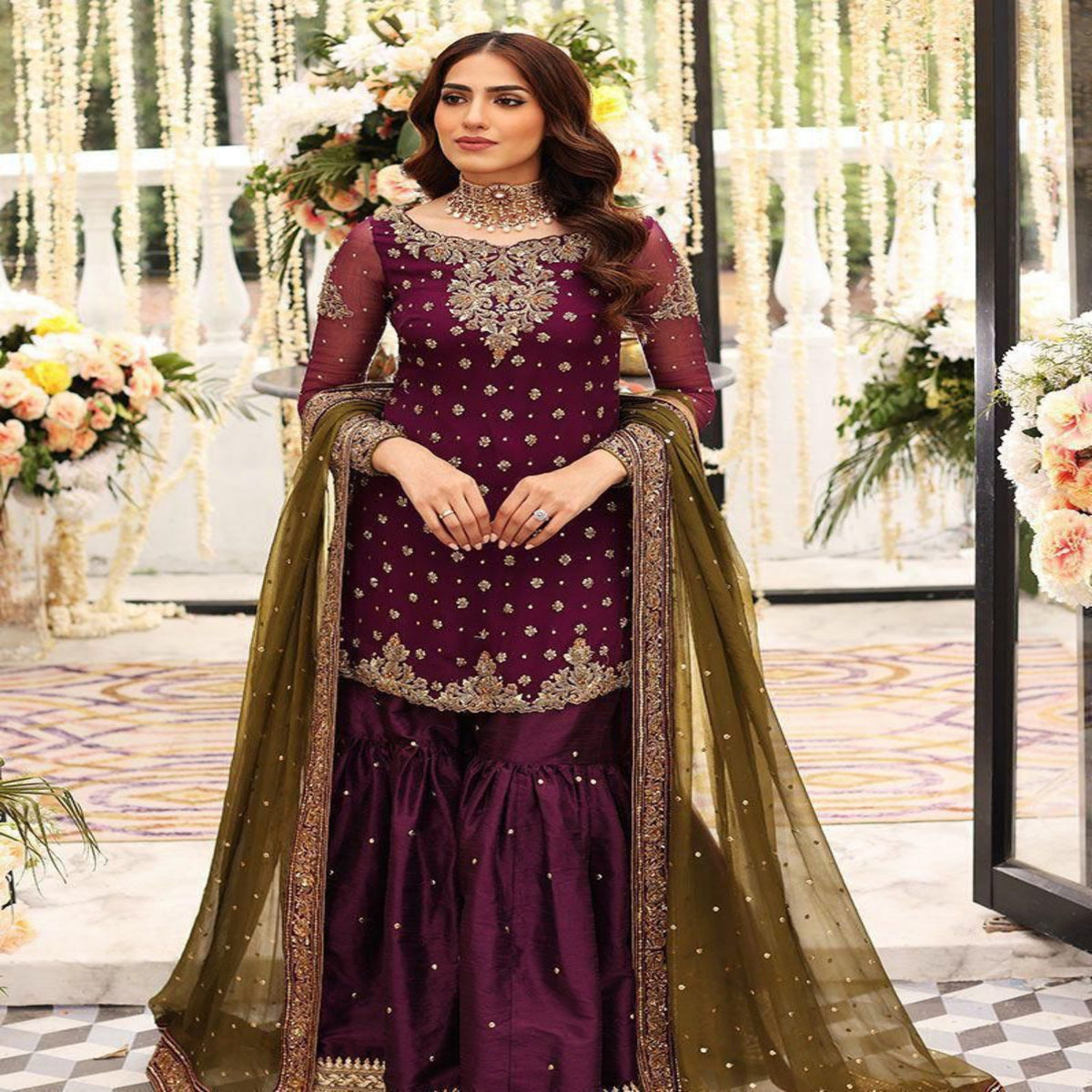 Woman in a purple and gold traditional outfit with floral decorations in the background