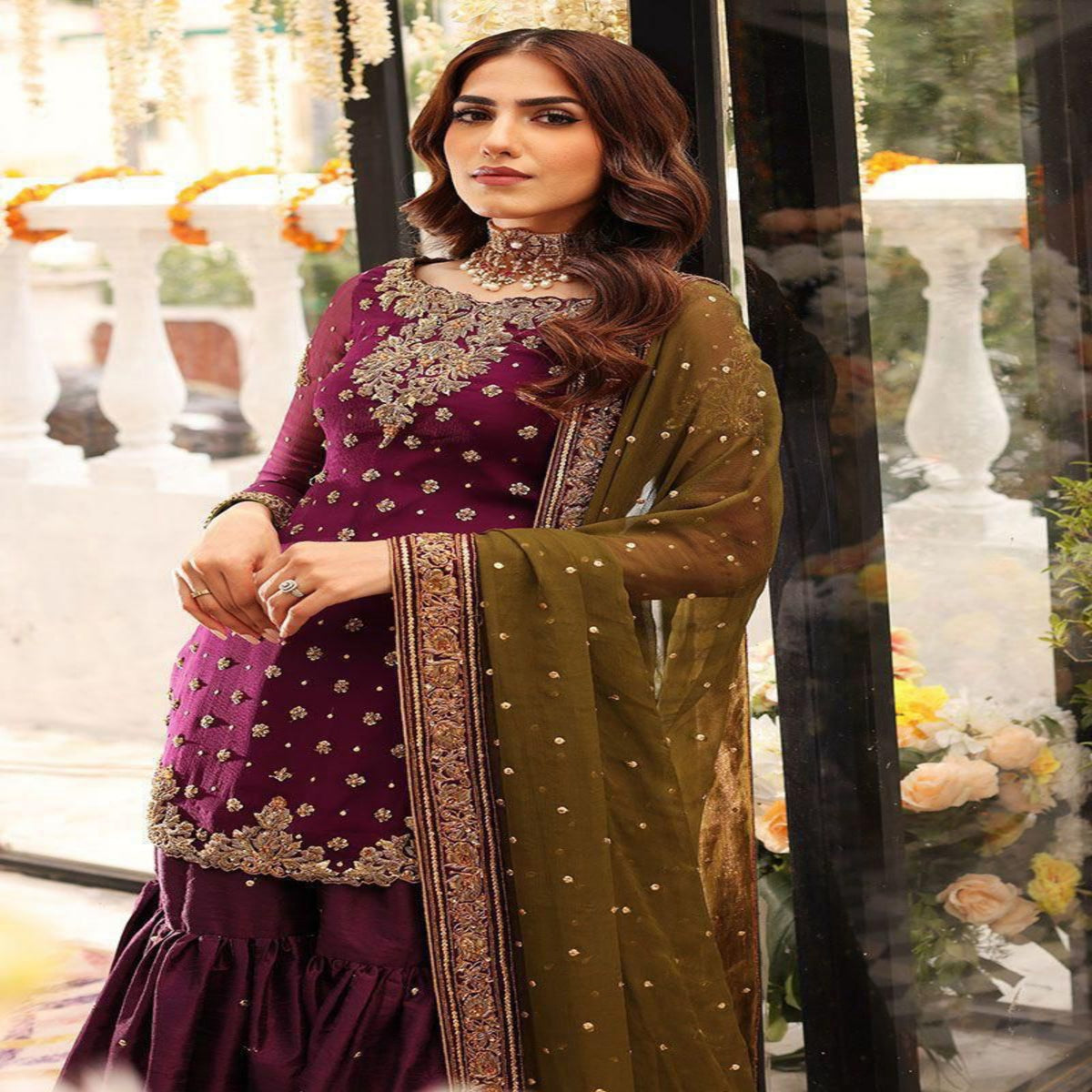 Woman in a purple and green traditional outfit with floral decorations in the background