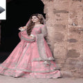 Woman in a pink embroidered traditional outfit standing against a stone wall.