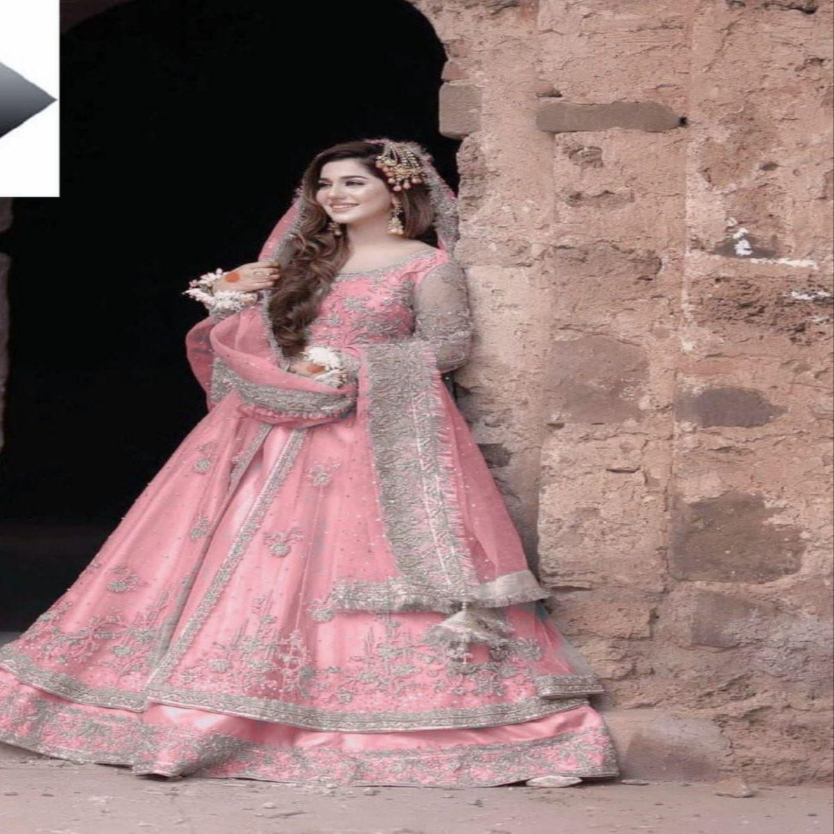 Woman in a pink embroidered traditional outfit standing against a stone wall.