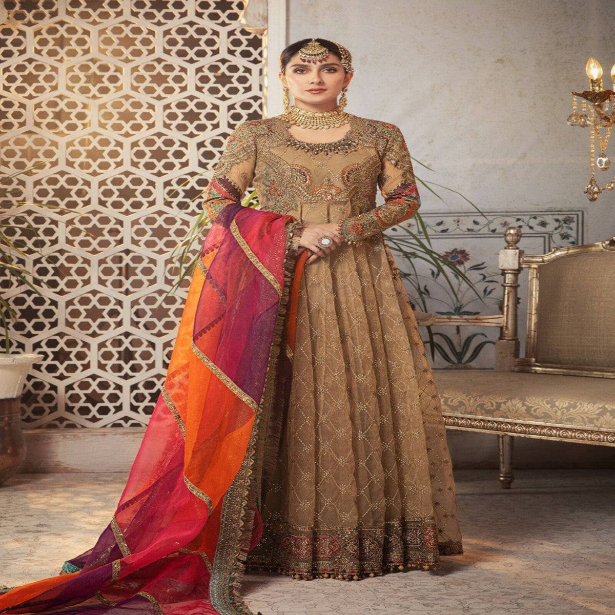 Woman in traditional embroidered outfit with a colorful dupatta in an ornate room.