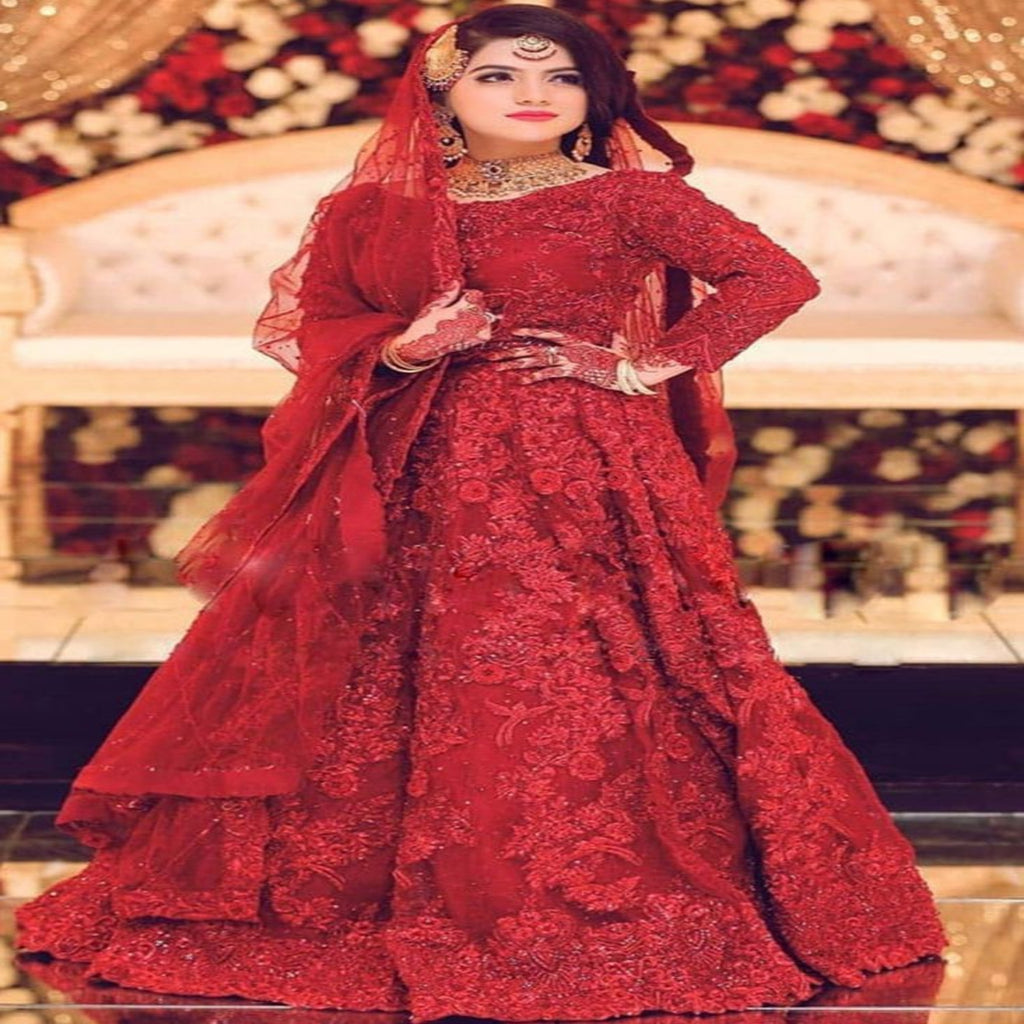 Woman in a red traditional outfit with intricate designs, standing in front of a decorated background.
