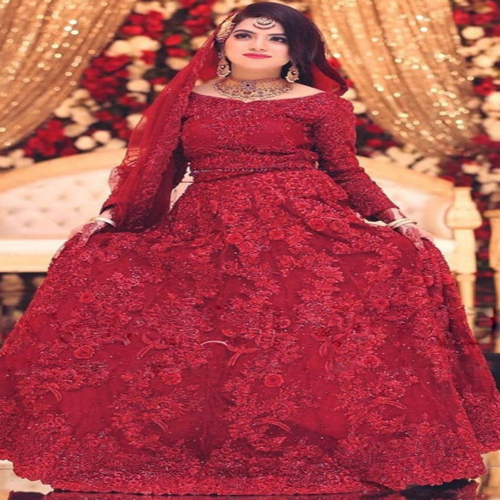 Woman in a red traditional outfit with intricate designs, sitting against a decorated background.