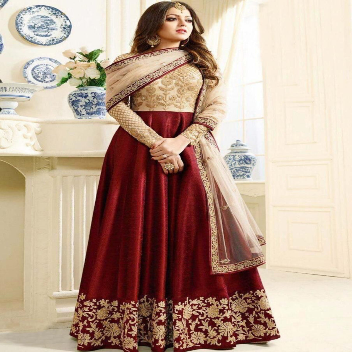 Woman wearing a traditional maroon and beige outfit in an elegant interior setting.