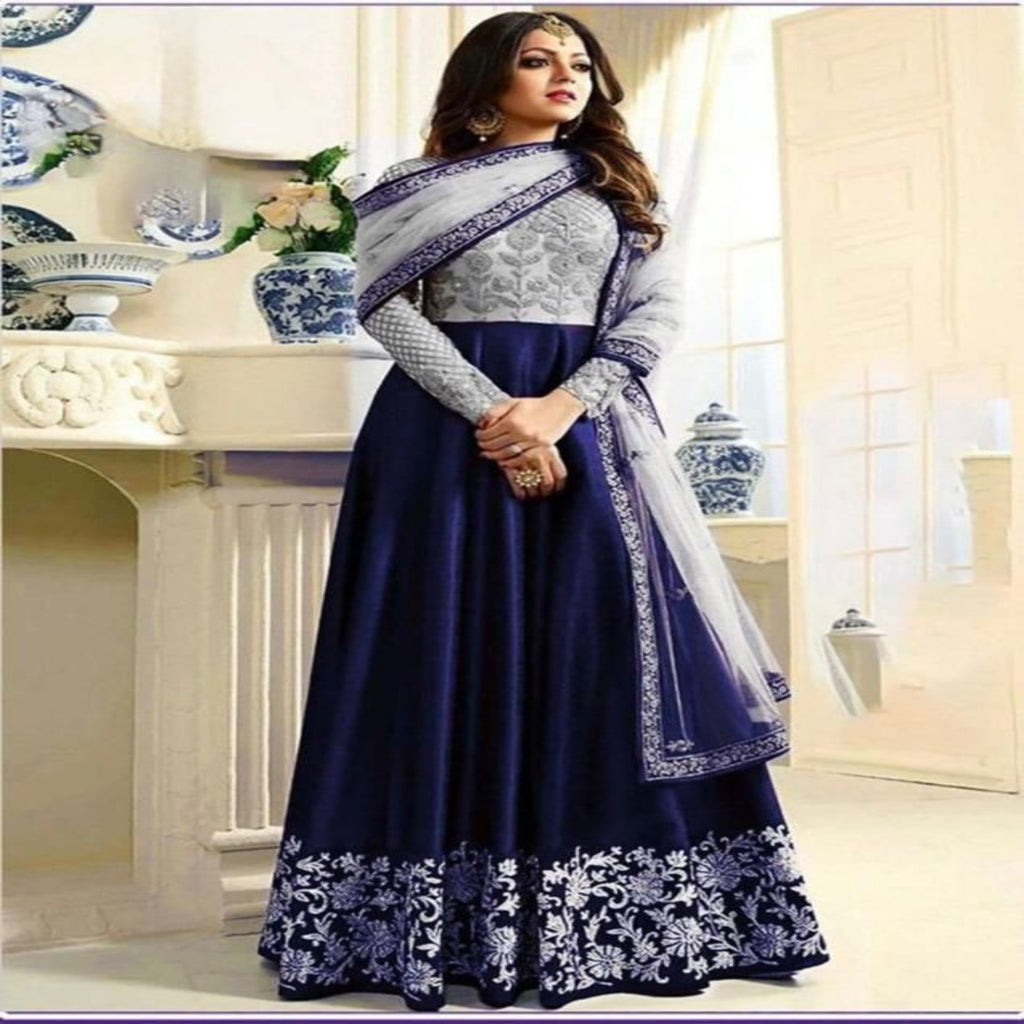 Woman wearing a blue and white embroidered traditional outfit in a decorated room.