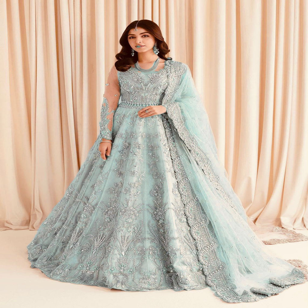 Woman in a light blue embroidered gown with a matching dupatta against a beige curtain background