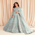 Woman in a light blue embroidered gown with a matching dupatta against a beige curtain background