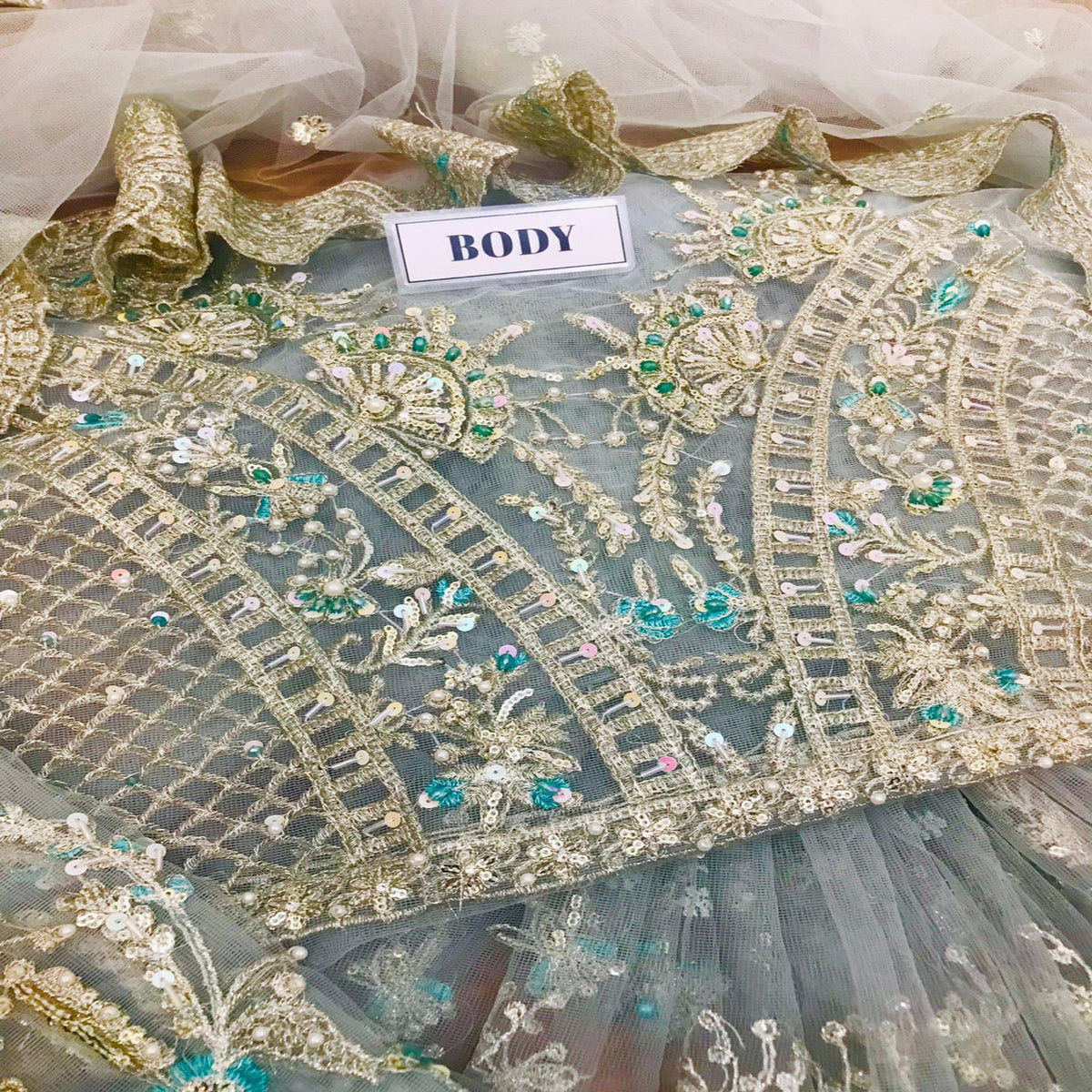 Decorative fabric with gold embroidery and green beads on a white background