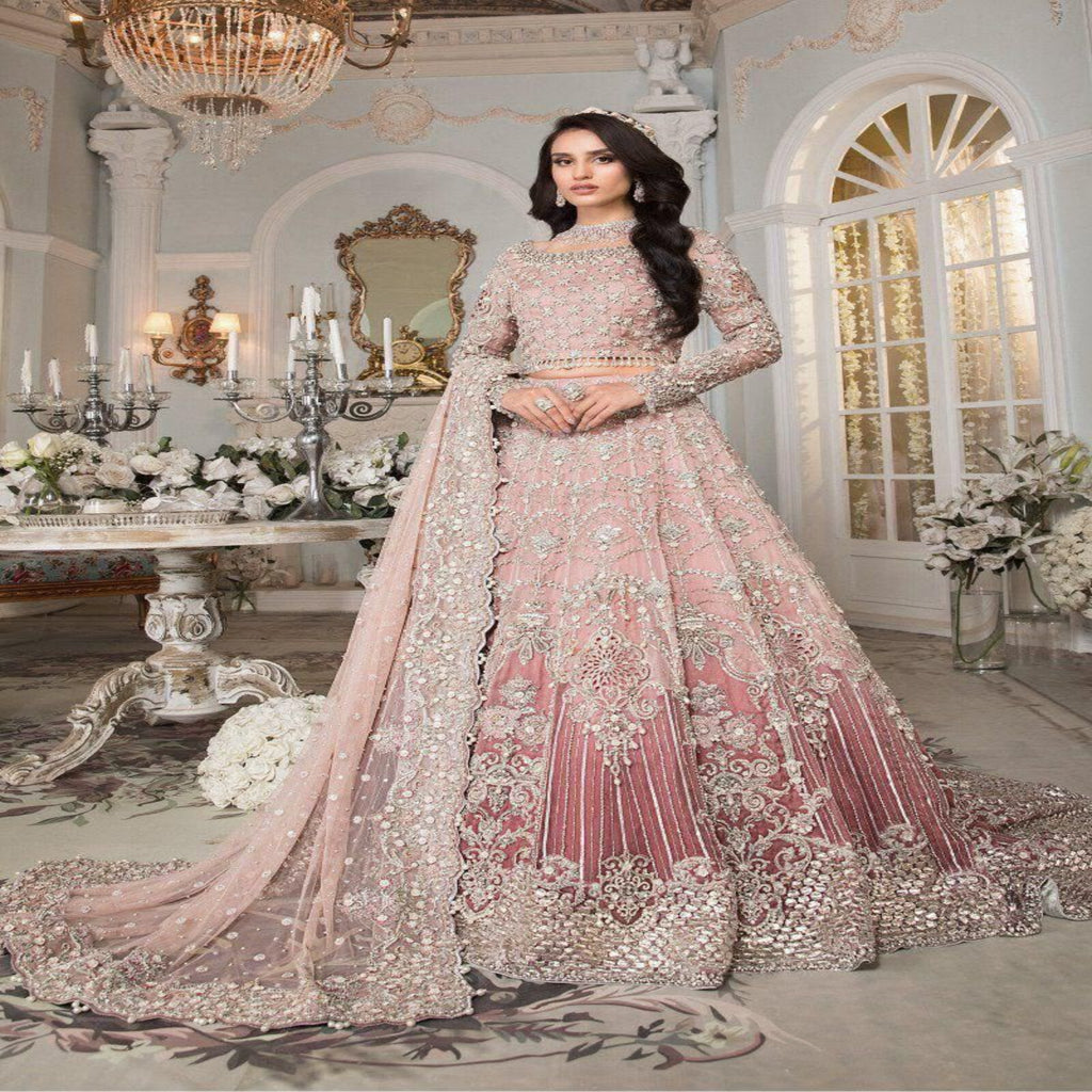Woman in a pink and gold traditional outfit in an elegant room with chandeliers and floral arrangements.