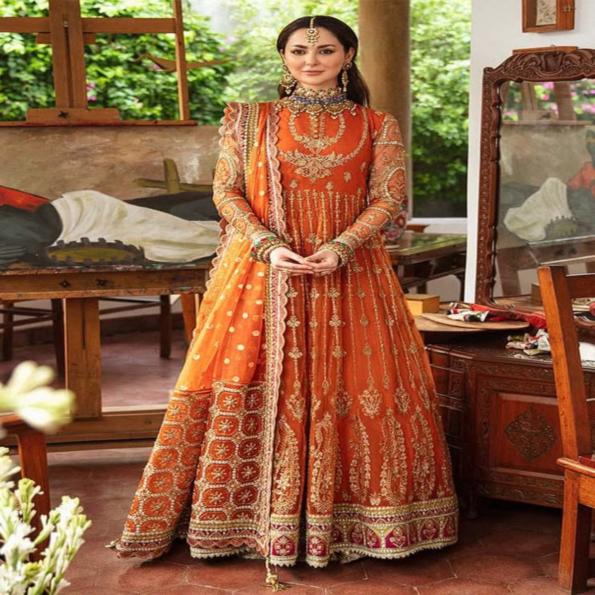 Woman in an orange and gold traditional outfit standing in a decorated room.