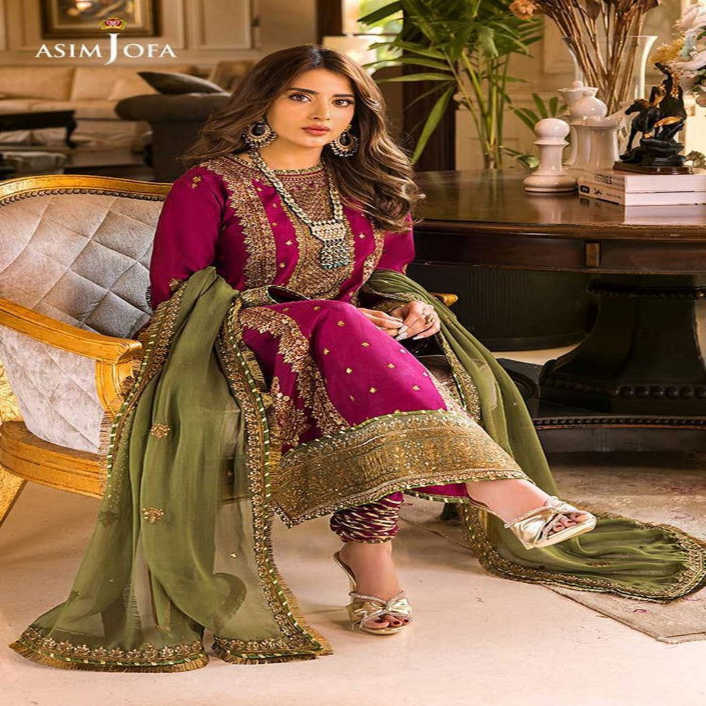 Woman in traditional pink and green embroidered outfit sitting in a luxurious room.