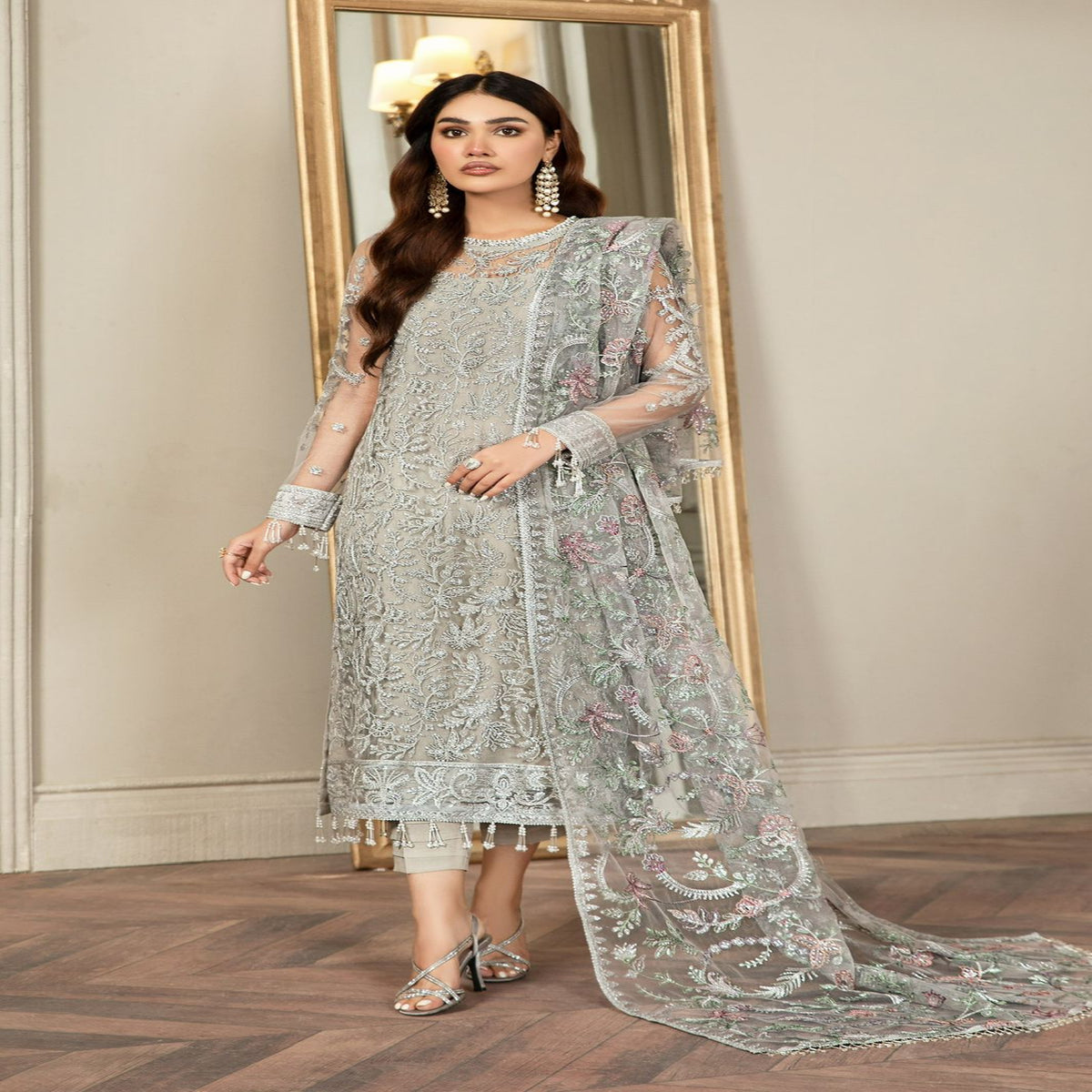 Woman in a light gray embroidered traditional outfit standing in front of a mirror.